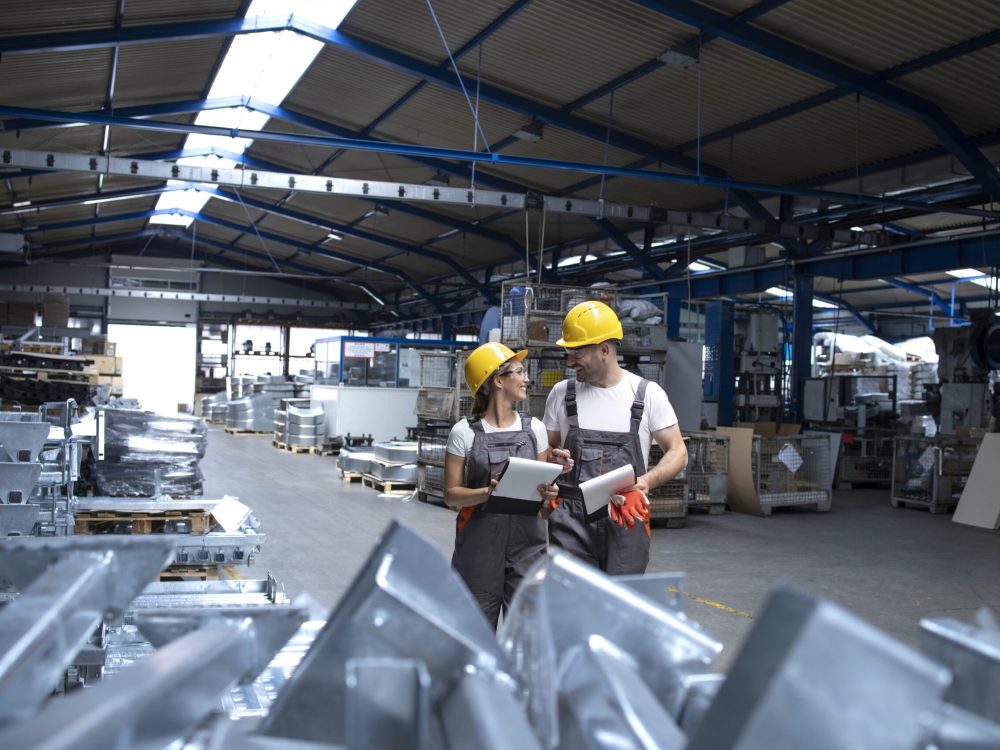 Factory workers in industrial production hall sharing ideas.